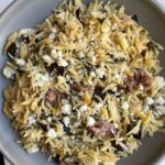 Grey bowl with orzo pasta, figs, prosciutto, and blue cheese.