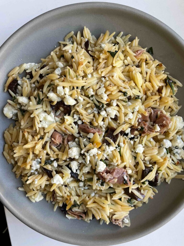 Grey bowl with orzo pasta, figs, prosciutto, and blue cheese.