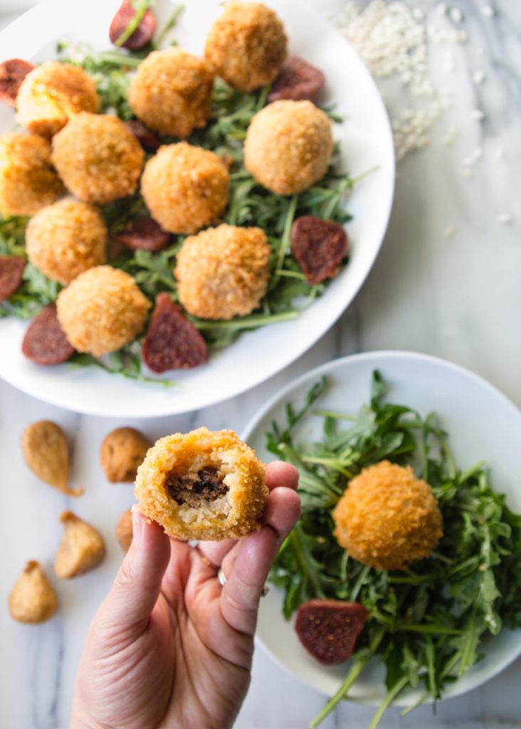 Arancini on a plate with a bite showing the inside of prosciutto, figs and mozzarella.