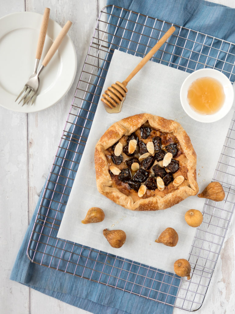 Fig galette with frangipane on a wire cooling rack with golden figs scattered around.