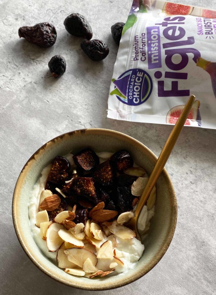Bowl of yogurt with sliced almonds and Orchard Choice California Dried Mission Figlets bag.