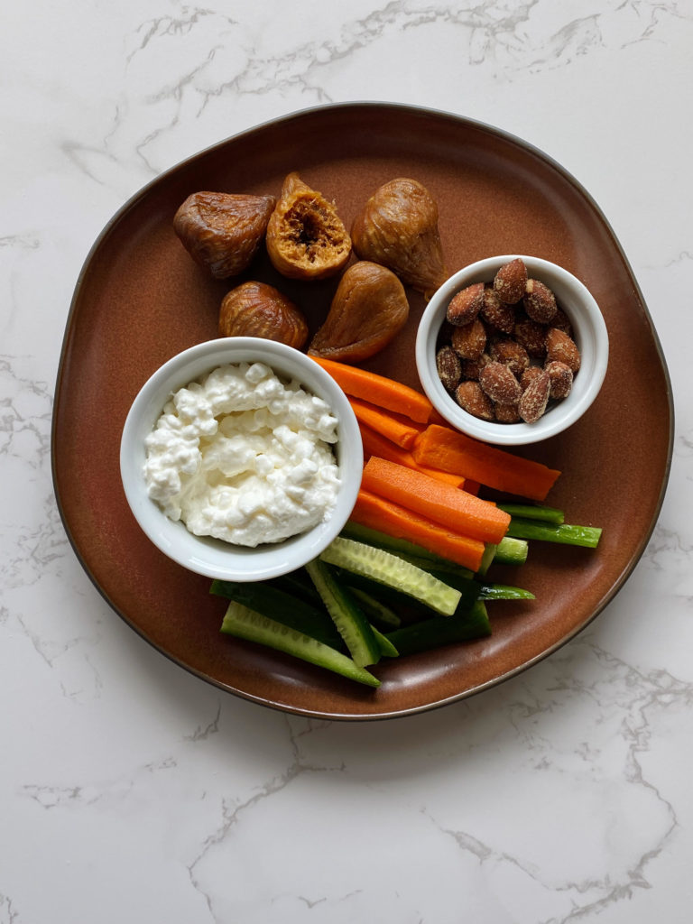 Plate of California Dried Golden Figs with cottage cheese, smoked almonds, carrots, and cucumbers.