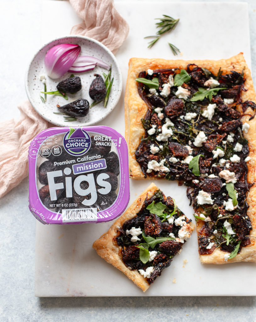 Goats cheese puff pastry with figs and caramelised onions on a marble board with a package of Orchard Choice Mission Figs.
