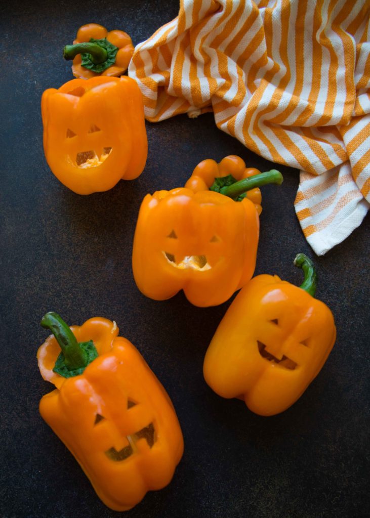 Orange bell peppers with carved jack o' lantern faces and an orange and white striped tea towel
