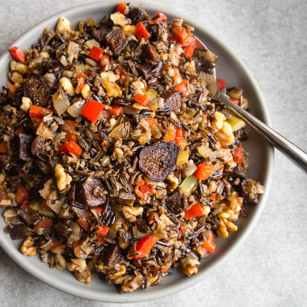 A serving bowl of wild rice dressing with figs set on a grey background
