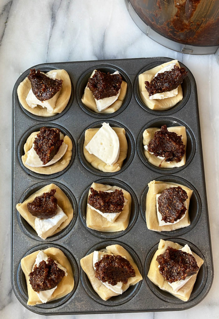 Mini muffin tin of unbaked mini brie bites with fig thyme jam