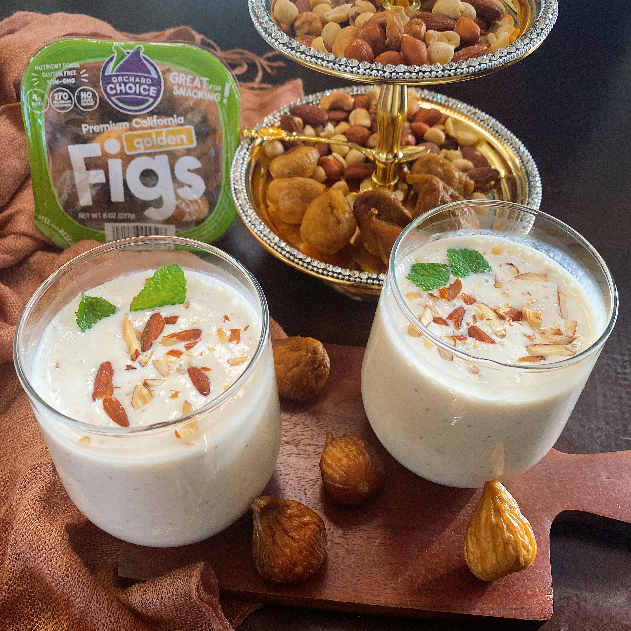 Two cups of fig lassi, a Yogurt drink with figs on a table surrounded by Golden Figs.
