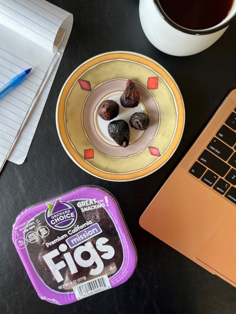 Orchard Choice Mission Fig packaging next to a plate of four figs for easy dried fig nutrition next to a computer and notepad with a pen: a simple snack provided 