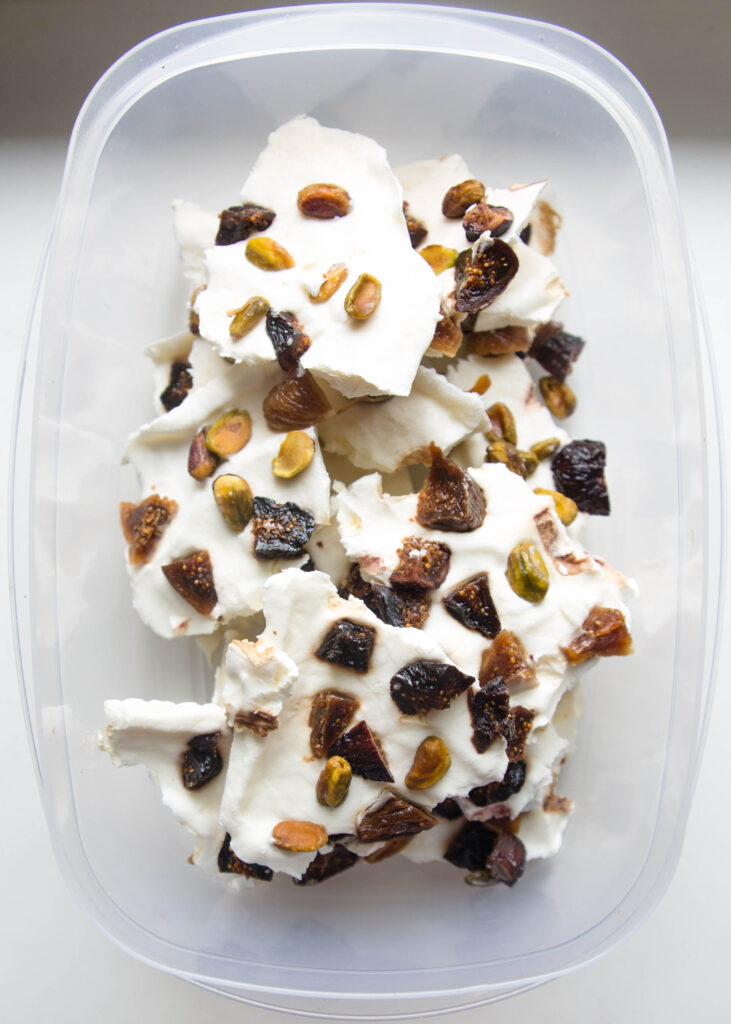 Tupperware of broken frozen labne bark with figs and pistachios