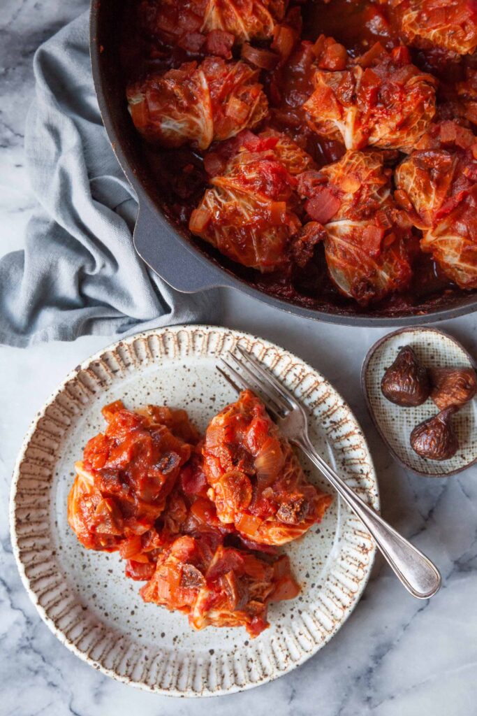Easy cabbage roll recipe photographed on a plate with a serving dish of cabbage rolls nearby.