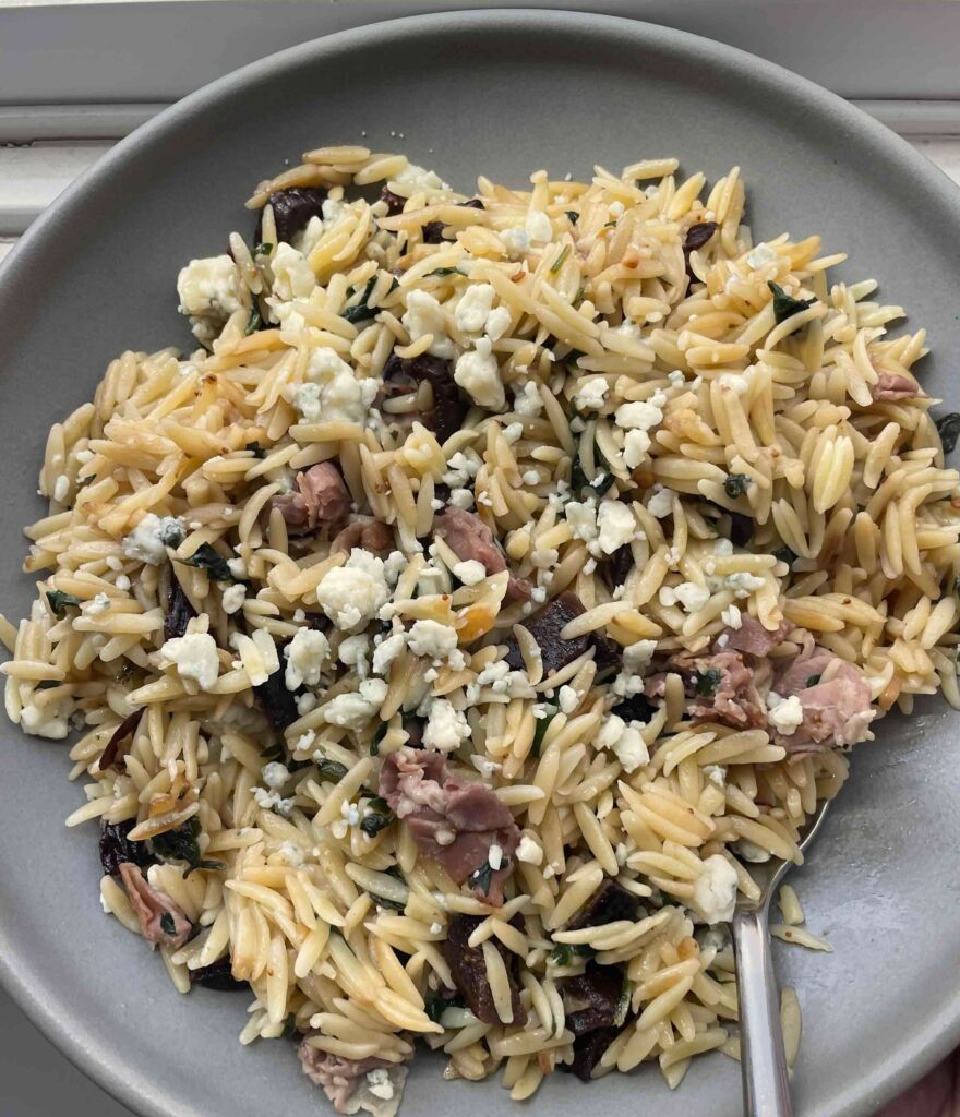 Grey bowl filled with orzo pasta recipe that has prosciutto, figs, and blue cheese