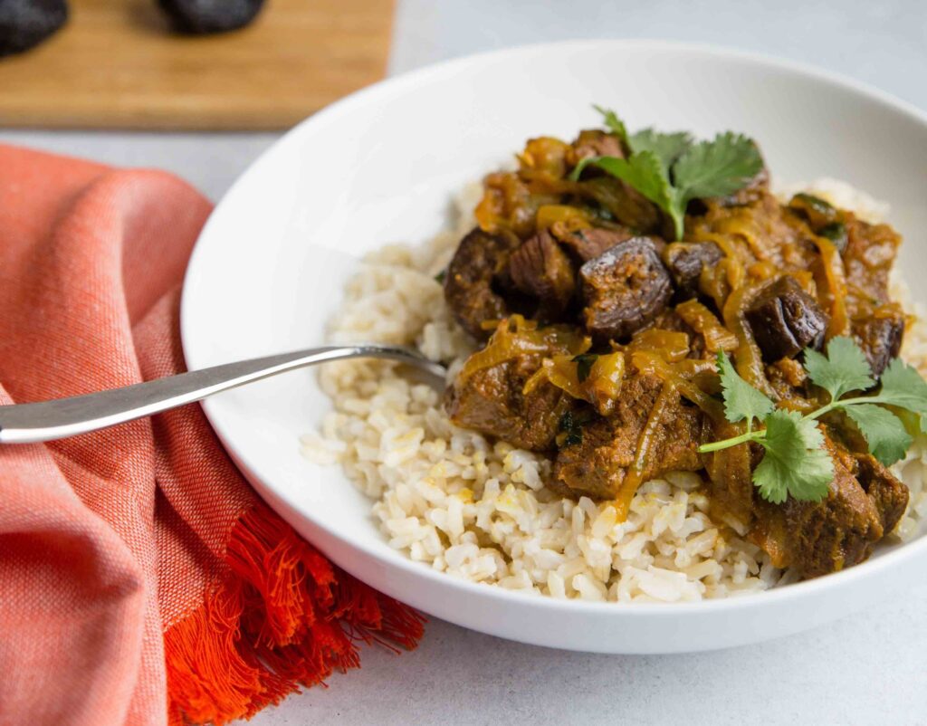 Lamb curry with figs over brown rice in a wide white bowl