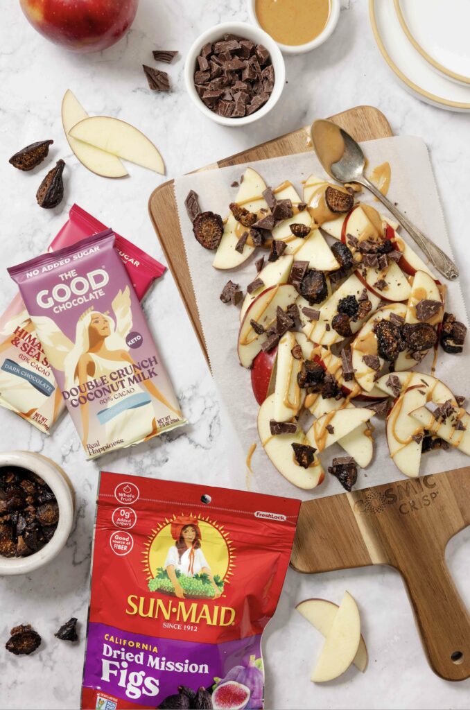recipe, apple nachos on a Cosmic Crisp wooden board with a bag of Mission Figs and bars of The Good Chocolate nearby.