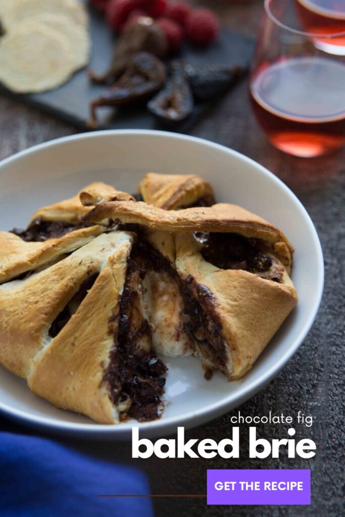 figs inside pastry with chocolate and brie on a white plate in front of glasses of rose wine